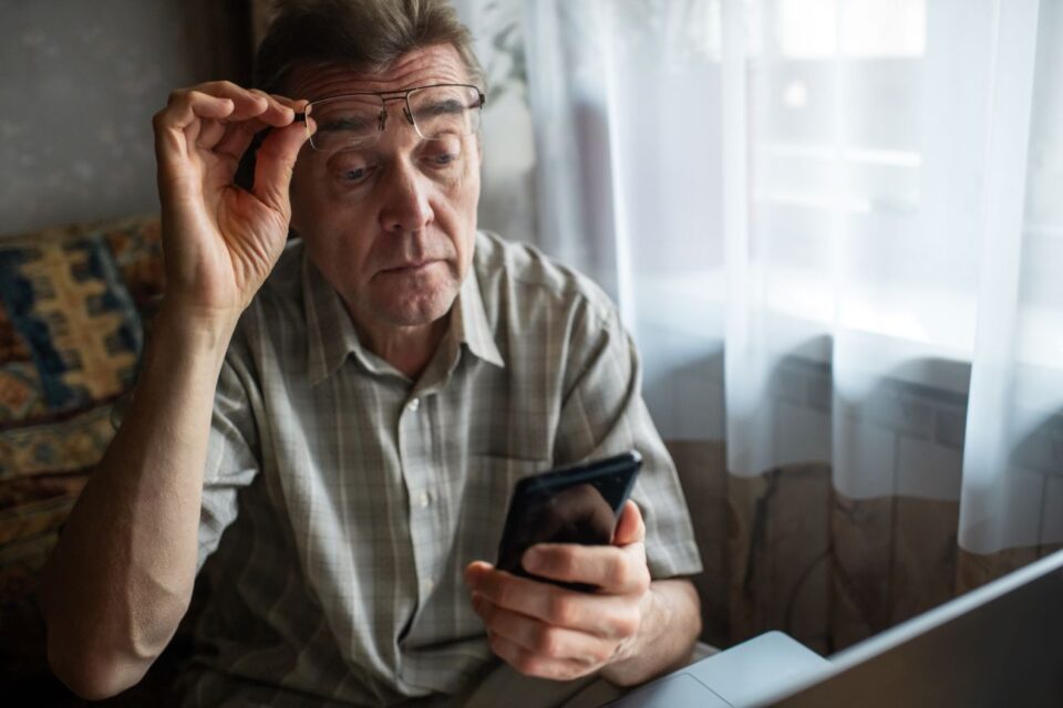 An elderly man holding a phone and adjusting his glasses to read in East Stroudsburg, PA